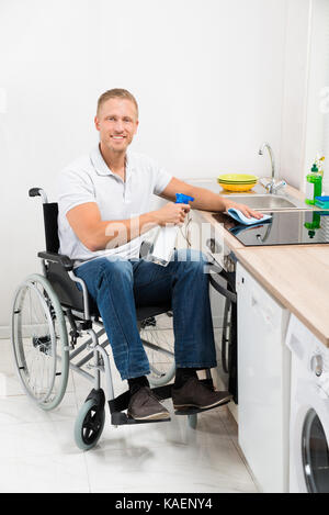 Jeune homme heureux sur Nettoyage de fauteuil roulant dans la salle de cuisine cuisinière à induction Banque D'Images