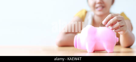 Asian woman putting money coin à pink piggy bank métaphore d'économiser de l'argent pour le ratio financier et de bannières web conception d'en-tête avec copie espace de faible profondeur Banque D'Images