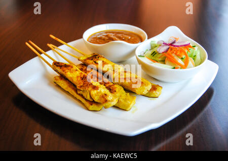 Satay de poulet, poulet mariné grillé sur des brochettes, servi avec sauce aux arachides et salade de concombre. Banque D'Images