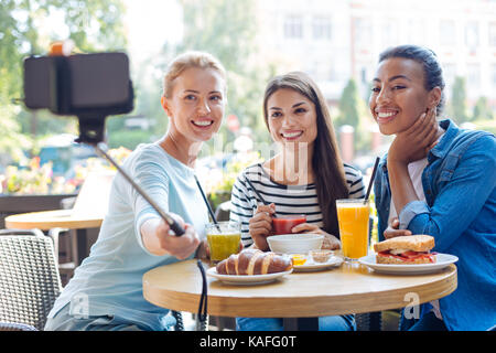 Les femmes prenant des autoportraits avec charme monopod in cafe Banque D'Images