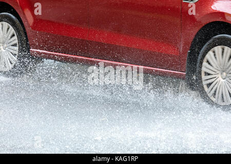 Voiture rouge roulant dans les flaques de pluie la création d'éclaboussures closeup Banque D'Images