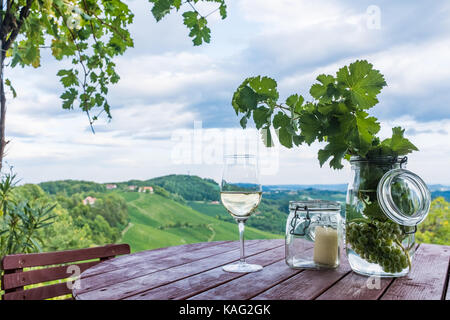 Vin blanc en verre et les bocaux avec les raisins et bougie sur tonneau en bois près de vignoble sur la route des vins du sud de la Styrie en Autriche Banque D'Images