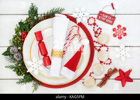 Table de noël place avec assiette, serviette, chapeau de Père Noël, des cannes de bonbon et de craquelins, petits pâtés, d'épices, de décorations, de houx, de cèdre, de lierre et de métis Banque D'Images