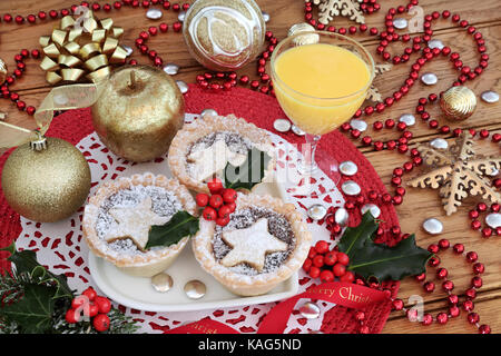 Petits pâtés de noël tartelettes avec de houx sur une plaque en forme de coeur avec du lait de poule, de l'or décorations babiole et perle rouge strand sur table en chêne, arrière-plan.. Banque D'Images