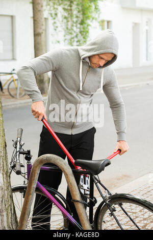 Voleur qui se briser le vélo de verrouillage garée près de la route Banque D'Images