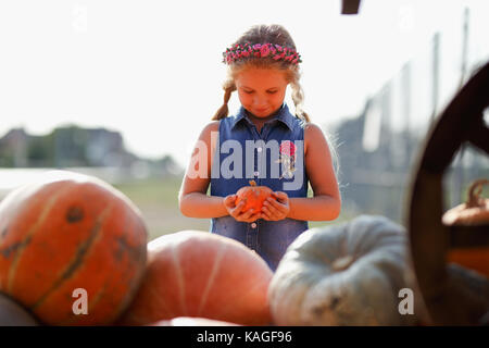 Happy school girl sitting entre citrouilles au marché fermier local dans la journée ensoleillée d'automne Banque D'Images