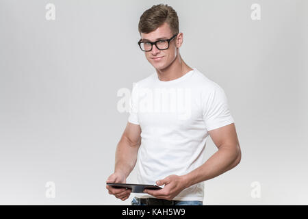 Handsome young man holding a tablet et souriant à la caméra. studio photo-shoot avec fond gris. Banque D'Images