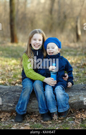 Deux enfants heureux ensemble avec de l'eau bouteille assis sur une grande forêt d'automne se connecter en toute sécurité avec une assurance vie pour les enfants. Banque D'Images