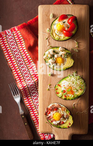 Oeufs cuits dans avocat avec bacon, fromage, tomates et germes de luzerne. Banque D'Images