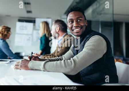 Young businessman sitting in réunion avec vos collègues en arrière-plan. Homme africain assis dans la salle du conseil. Banque D'Images