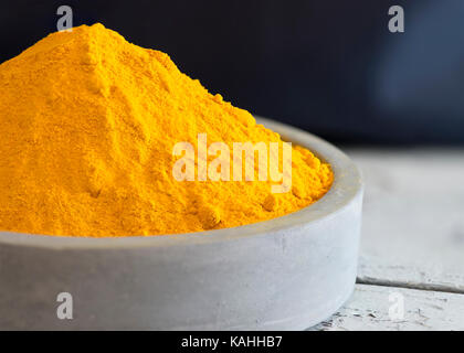 Macro close up shot de poudre de curcuma dans une pile dans un plat de céramique bleu clair avec un fond sombre copie espace à côté d'en-tête et Banque D'Images