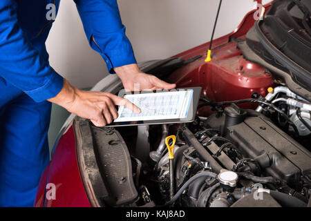 Close-up of mechanic using digital tablet lors de l'examen du moteur de voiture en garage Banque D'Images