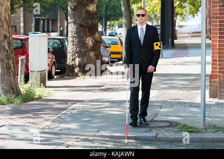 Blind Man Walking on Sidewalk Holding Stick Wearing Armband Banque D'Images
