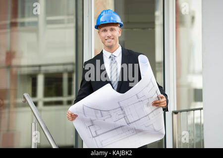 Jeune ingénieur With Hard Hat Holding Plan Directeur dans ses mains Banque D'Images