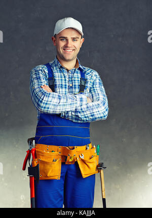 Portrait of happy young male construction worker avec ceinture d'outils ,contre mur texturé gris Banque D'Images