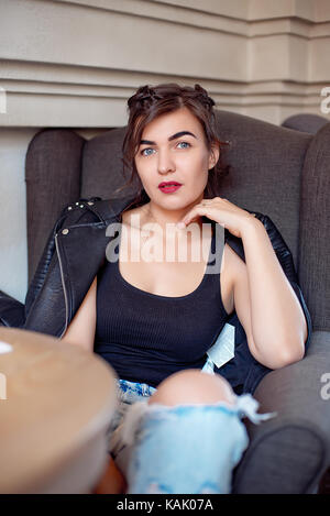 Femme assise dans un fauteuil à l'intérieur café moderne portant en jeans et blouson de cuir. Banque D'Images