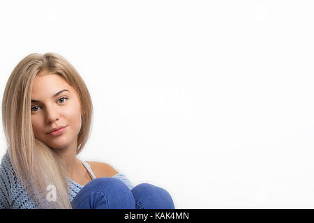 Portrait d'une jeune fille adolescente nice assis en jean et pull , pendant qu'elle recherche dans l'appareil photo, isolé sur blanc, copy space Banque D'Images
