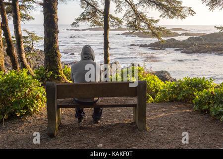 Homme assis sur banc avec vue sur la mer sur l'île de Vancouver au coucher du soleil Banque D'Images