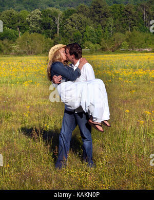 Profitez de quelques moment romantique dans le champ de fleurs jaunes. homme femme tient dans ses bras et l'embrasse alors qu'il porte sa à travers un champ de l'Alabama. Banque D'Images