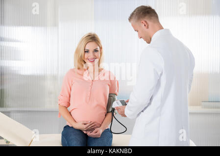 Doctor smiling contrôle la pression artérielle de la femme enceinte à l'hôpital Banque D'Images