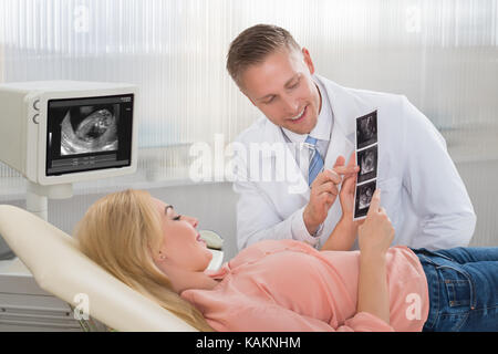 Jeune homme médecin expliquant échographie de femme enceinte à l'hôpital Banque D'Images