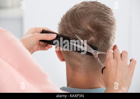 Vue arrière du jeune homme se coupe au salon de coiffure Femme Banque D'Images