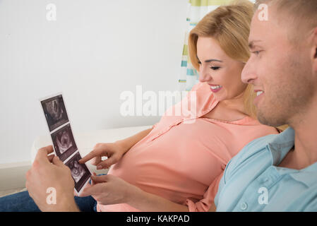 Jeune femme enceinte couple échographie rapport sur canapé à la maison Banque D'Images