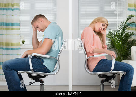 Vue latérale sur toute la longueur de colère jeune couple assis sur des chaises à la maison Banque D'Images