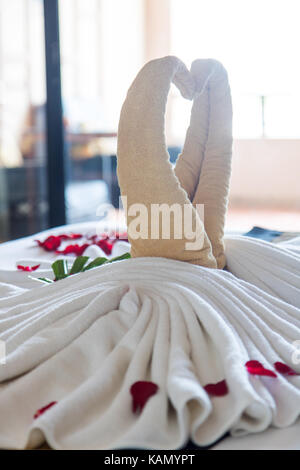 Les oiseaux de décoration avec des pétales de rose rouge sur blanc nettoyer lit dans chambre d'hôtel avec rétro-éclairage. Banque D'Images