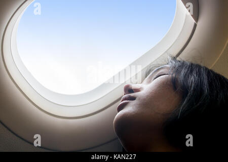 Portrait d'une jeune fille se reposant sur un avion. Une jeune femme dormant dans une fenêtre d'un avion en vol. rêver dans les nuages. Banque D'Images