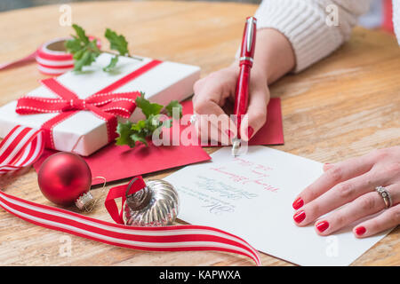 Jeune femme écrit cartes de Noël avec des clous rouges, un stylo rouge, et des décorations de Noël sur une table en bois Banque D'Images