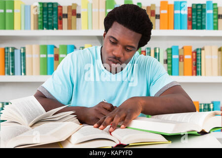 Young male university student studying at desk in library Banque D'Images