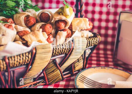 Panier en osier avec mini hot dog (maison de la saucisse dans la pâte) et d'une soucoupe avec une fourche sur un fond à carreaux Banque D'Images