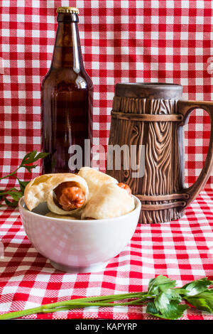 Mini plaque de maison hot dog (saucisse en croûte) sur serviette avec une bouteille de bière brune et faïence mug sur un fond à carreaux Banque D'Images