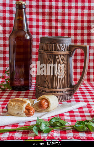 Mini maison hot dog (saucisse en croûte) sur serviette avec une bouteille de bière brune et faïence mug sur un fond à carreaux Banque D'Images