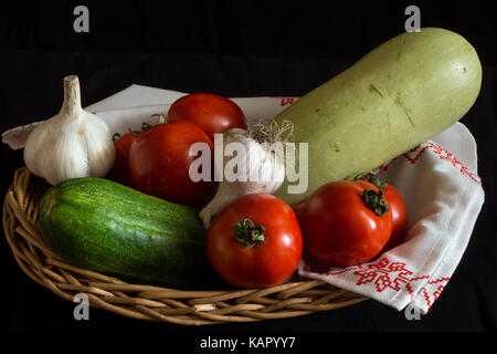 Légumes panier en osier sur un fond noir : courgettes, tomates, ail et concombre. Banque D'Images