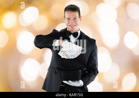 Portrait of young magician montrant tour avec des cartes à jouer contre l'arrière-plan lumineux Banque D'Images