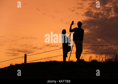 Un couple silhouette sur le coucher du soleil sur le mont stanserhorn, près de Engelberg, Suisse. Les deux sont à l'aide de leurs téléphones portables avec appareil photo intelligent. Banque D'Images