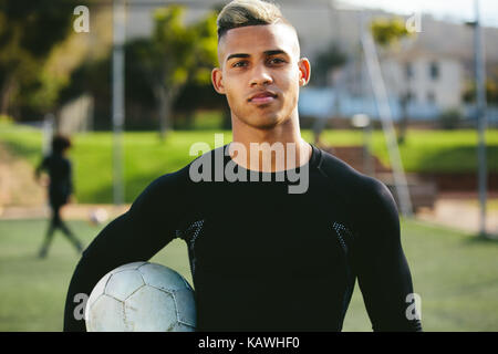 Portrait of teenage soccer player holding a football dans sa main et en regardant la caméra. Jeune homme au cours de la formation sur terrain de football. Banque D'Images