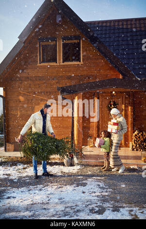 Les parents d'enfant portant des cadeaux et le feu pour Noël dans la maison en bois Banque D'Images