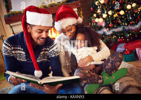 Les jeunes de la famille afro lecture contes de Noël près de cheminée Banque D'Images