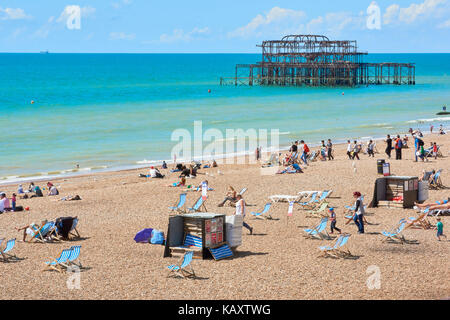 Amateurs de profiter du soleil à Brighton, endommagée par l'incendie avec Brighton West Pier squelette dans l'arrière-plan. Banque D'Images