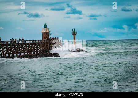 C'est une qualité d'image d'une scène de la mer avec une jetée, phare, le fracas des vagues, des rochers et un ciel bleu avec des nuages qui complètent l'image. Banque D'Images