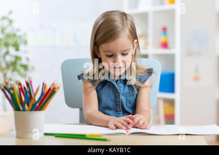 Petit enfant fille attire l'assis à table dans la salle à la maternelle Banque D'Images