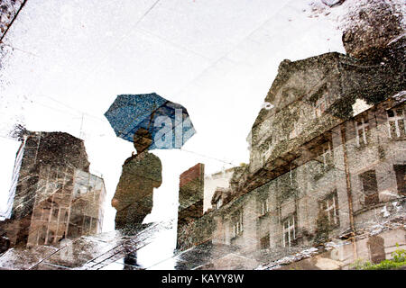 Ombre de réflexion silhouette d'une personne sous parapluie et un bâtiment dans la flaque Banque D'Images