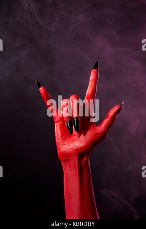 La main du diable rouge avec noir ongles pointus, studio shot sur fond fumé Banque D'Images