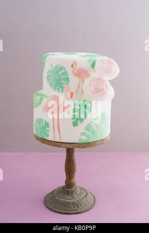 Gâteau de mariage tropical à deux niveaux avec du fondant, le pain azyme tropicales et des flamants roses avec feuilles ranunculus flowers on cake stand en bois Banque D'Images