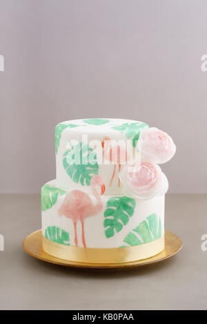 Gâteau de mariage tropical à deux niveaux avec du fondant, le pain azyme tropicales et des flamants roses avec feuilles ranunculus fleurs sur le plateau de cale d'or Banque D'Images