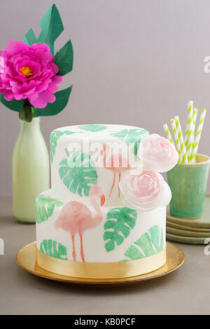 Gâteau de mariage tropical à deux niveaux avec du fondant, le pain azyme tropicales et des flamants roses avec feuilles ranunculus fleurs sur le plateau de cale d'or Banque D'Images