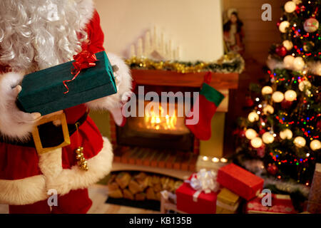 Le père Noël dans les mains gantées holding gift box next Christmas Tree Banque D'Images